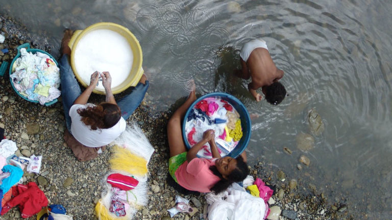 Några kvinnor tvättar kläder i en flod och ett barn badar.